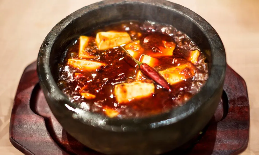 Spicy mapo tofu simmering in a stone pot with chili oil at Lucky Dumplings, a Dumpling Restaurant in Great Neck
