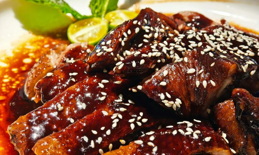 Glazed teriyaki pork slices with sesame seeds and lime garnish at Lucky Dumplings, a Dumpling Restaurant in Great Neck